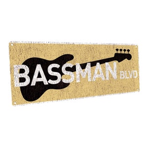 May include: A tan and white sign with a black silhouette of a bass guitar and the text "BASSMAN BLVD".