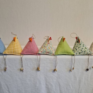 May include: Seven fabric chicken decorations with triangular bodies and dangling legs. Each chicken is made from a different patterned fabric, such as polka dots, gingham, and floral prints. They have orange beaks and small wooden bead details.
