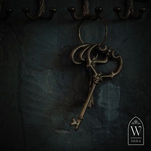 May include: A set of antique keys with intricate designs hanging on hooks against a dark, textured wall. The keys are made of metal and have a rustic, aged appearance.