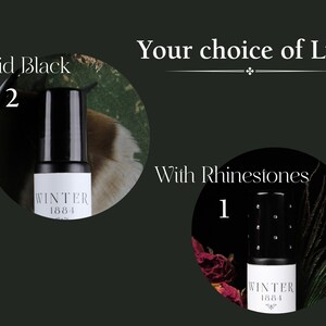 May include: Two black roll-on bottles with the text "WINTER 1884" on the label. The bottle on the left has a solid black lid. The bottle on the right has a lid with rhinestones. The text "Your choice of Lid" is above the bottles. The text "Solid Black" is above the bottle on the left. The text "With Rhinestones" is above the bottle on the right.