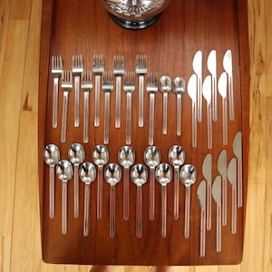 May include: A set of silver cutlery, including forks, spoons, and knives, arranged on a wooden surface. The cutlery is arranged in rows, with the forks on the left, the spoons in the middle, and the knives on the right.