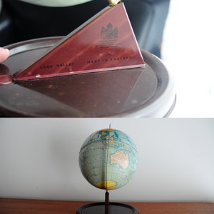 May include: A vintage globe with a blue and green map of the world. The globe is on a black stand with a wooden base. The globe is made by Chad Valley and says "Made in England".