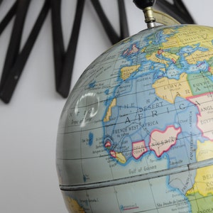 May include: A vintage globe with a blue and yellow map of the world. The globe is made of plastic and has a metal stand. The globe is tilted at an angle, showing the continents of Africa, Europe, and Asia.
