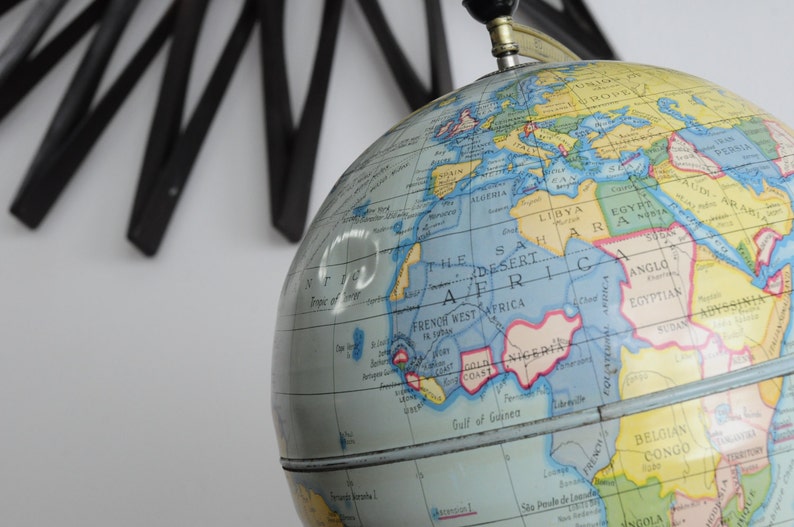 May include: A vintage globe with a blue and yellow map of the world. The globe is made of plastic and has a metal stand. The globe is tilted at an angle, showing the continents of Africa, Europe, and Asia.