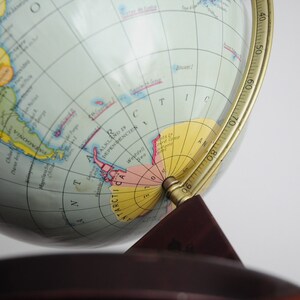 May include: A vintage globe with a brass meridian and a wooden base. The globe shows the continents in different colors and includes a detailed map of Antarctica.