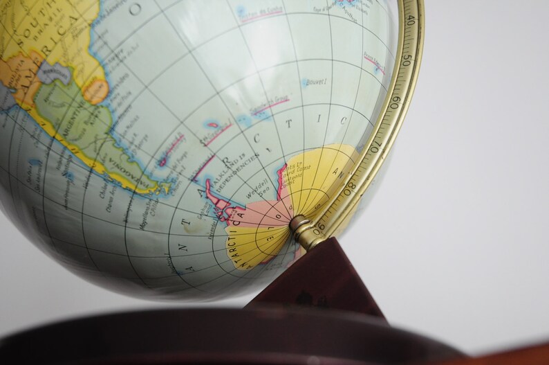 May include: A vintage globe with a brass meridian and a wooden base. The globe shows the continents in different colors and includes a detailed map of Antarctica.