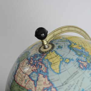May include: A vintage globe with a blue and yellow map, a gold meridian ring, and a black knob for rotating the globe.