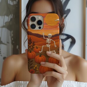 以下が含まれることがあります： ハロウィーンをテーマにしたデザインの携帯電話ケース。オレンジ、茶色、黄色の色合いで、スケルトン、カボチャ、夕焼けの風景が描かれています。このデザインは、秋の季節にぴったりの気まぐれなイラストです。