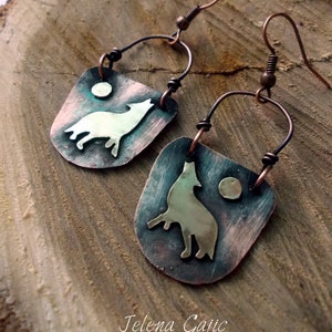 May include: A pair of copper earrings with a wolf silhouette and a moon design. The earrings are handmade and have a rustic, vintage look.