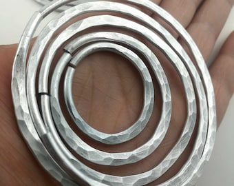 May include: A set of five silver metal rings, each with a hammered texture, are stacked on top of each other. The rings are all different sizes, with the largest ring at the bottom and the smallest ring at the top.