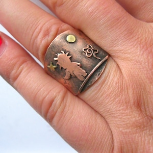 Könnte beinhalten: Ein Kupferring mit einer Silhouette einer Person mit einem Stern- und Blumendesign. Der Ring hat eine strukturierte Oberfläche und einen goldenen Akzent.