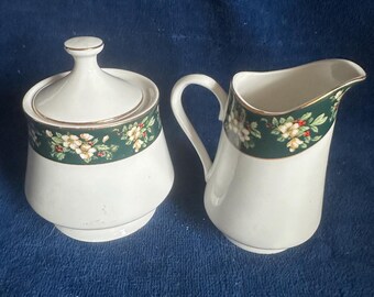 May include: A white ceramic creamer and sugar bowl set with a green and white floral design and gold trim. The set is perfect for serving coffee or tea.