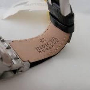 May include: Close-up of a black leather watch band with the Invicta Reserve logo embossed in silver.