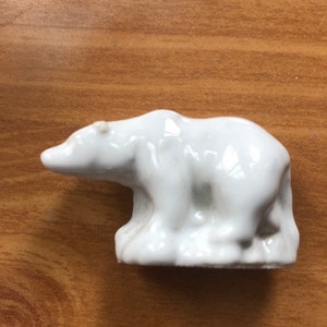 May include: White ceramic figurine of a polar bear standing on a base. The bear is facing left and has a smooth, glossy finish.