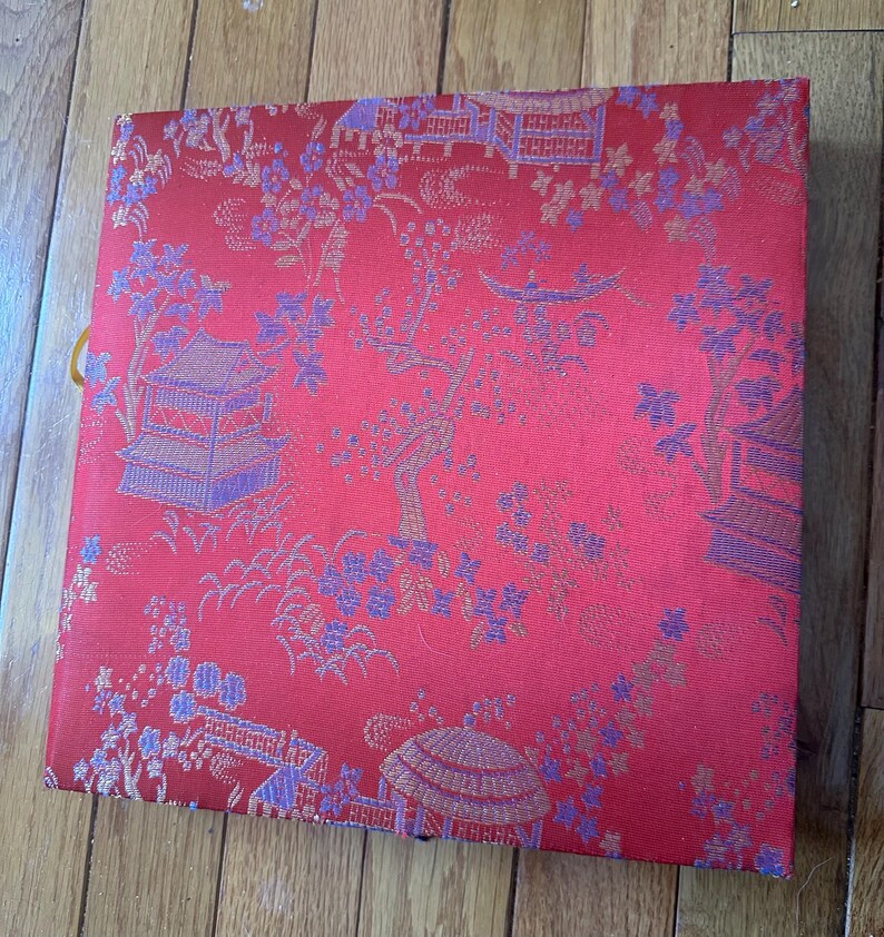 May include: A red box with a gold and purple floral pattern. The box has a gold trim and a gold tassel.