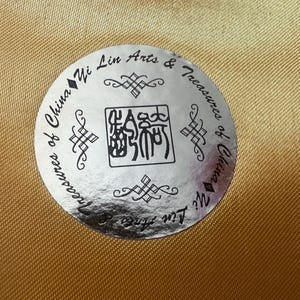 May include: A silver sticker with black text and a black Chinese character. The text reads "Treasures of China Yi Lin Arts & Treasures of China Yi Lin".