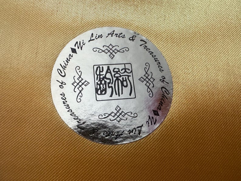 May include: A silver sticker with black text and a black Chinese character. The text reads "Treasures of China Yi Lin Arts & Treasures of China Yi Lin".
