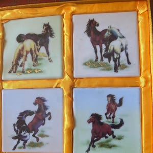 May include: A set of four square ceramic coasters with images of horses. The coasters are in a yellow box with a red lining. The horses are depicted in various poses, including running, standing, and jumping. The coasters are a great way to add a touch of elegance to your home decor.