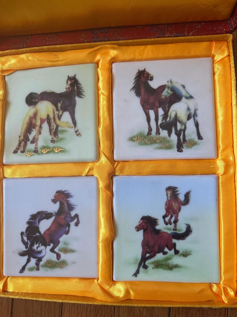 May include: A set of four square ceramic coasters with images of horses. The coasters are in a yellow box with a red lining. The horses are depicted in various poses, including running, standing, and jumping. The coasters are a great way to add a touch of elegance to your home decor.