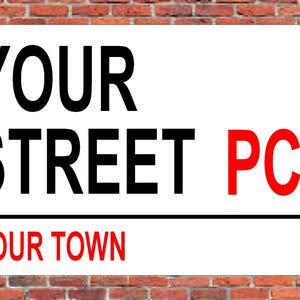 May include: White sign with black text that reads "YOUR STREET PC1 YOUR TOWN". The text "PC1" is in red.