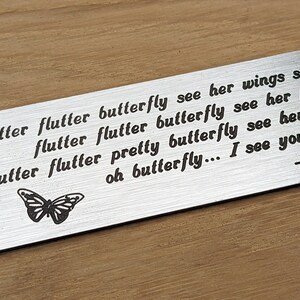 May include: A silver metal plaque with a butterfly design and the text "Flutter flutter butterfly see her wings sparkle flutter flutter butterfly see her pass y flutter flutter pretty butterfly see her twing oh butterfly... I see you there -Mary"