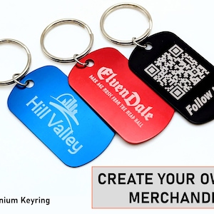 May include: Three aluminium keyrings with different designs. The first keyring is blue with the text "Hill Valley" and a graphic of a city skyline. The second keyring is red with the text "Elven Dale" and the text "DARK AGE MUSIC FROM THE MEAD HALL". The third keyring is black with a QR code and the text "Follow us!"
