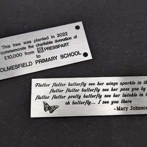 May include: Two silver metal plaques with engraved text. The top plaque commemorates a charitable donation of &pound;10,000 from PRESSPART to HOLMESFIELD PRIMARY SCHOOL. The bottom plaque features a butterfly graphic and a poem about a butterfly.