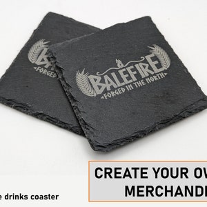 Op de afbeelding: Twee zwarte leisteen onderzetters met een wit gegraveerd ontwerp. Het ontwerp bevat een tarwehalm en de tekst "BALEFIRE FORGED IN THE NORTH".