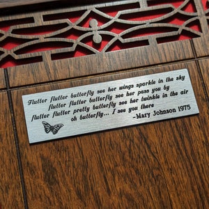 May include: A wooden plaque with a silver metal insert featuring a poem about a butterfly. The poem reads: "Flutter flutter butterfly see her wings sparkle in the sky flutter flutter butterfly see her pass you by flutter flutter pretty butterfly see her twinkle in the air oh butterfly... I see you there -Mary Johnson 1975"