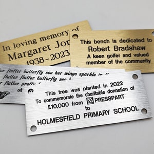 May include: Three engraved metal plaques with different messages. The top plaque is gold and reads "In loving memory of Margaret Jor 1938-2023". The middle plaque is silver and reads "Flutter flutter butterfly see her wings sparkle in... flutter flutter butterfly see... flutter flutter preff... oh". The bottom plaque is silver and reads "This tree was planted in 2022 To commemorate the charitable donation of &pound;10,000 from PRESSPART to HOLMESFIELD PRIMARY SCHOOL".