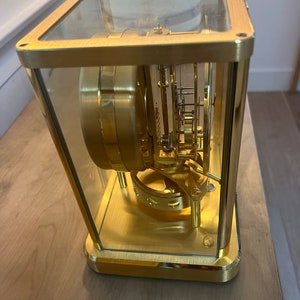 K&ouml;nnte beinhalten: Eine goldfarbene Uhr mit einem Glasgeh&auml;use, das die komplizierten inneren Mechanismen freilegt.