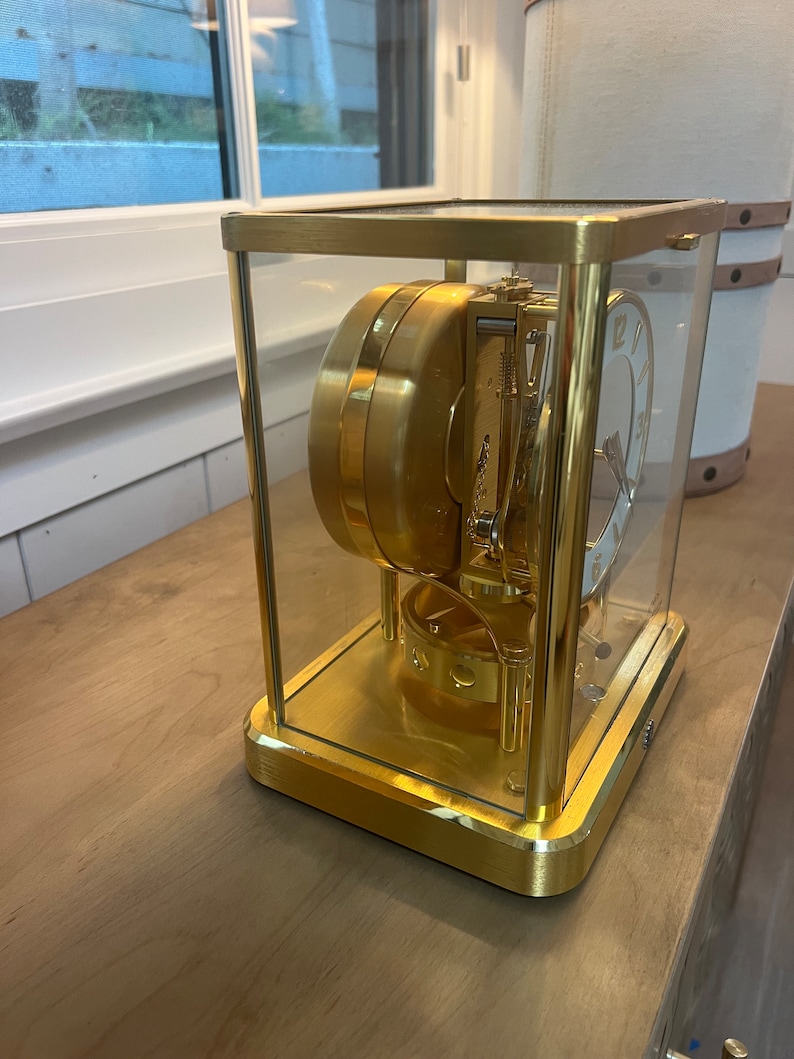 K&ouml;nnte beinhalten: Eine goldfarbene Uhr mit einem Glasgeh&auml;use, das die komplizierten inneren Mechanismen des Uhrwerks zeigt. Das Zifferblatt der Uhr hat r&ouml;mische Ziffern und einen wei&szlig;en Hintergrund.