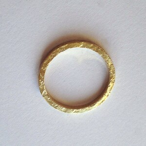May include: A gold ring with a textured finish. The ring is circular and made of gold. The ring is set against a white background.
