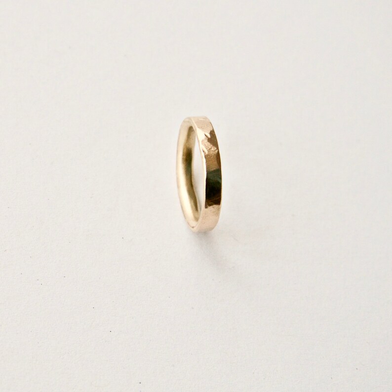 May include: A gold-coloured ring with a hammered texture. The ring is a simple band design, suitable for everyday wear. The ring is shown against a white background.