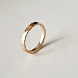 May include: A gold ring with a hammered texture. The ring is circular and appears to be made of metal. The ring is set against a white background, with a shadow cast to the right.