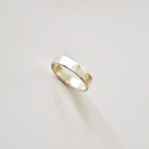 May include: A silver hammered band ring. The ring is smooth and has a slightly textured surface.