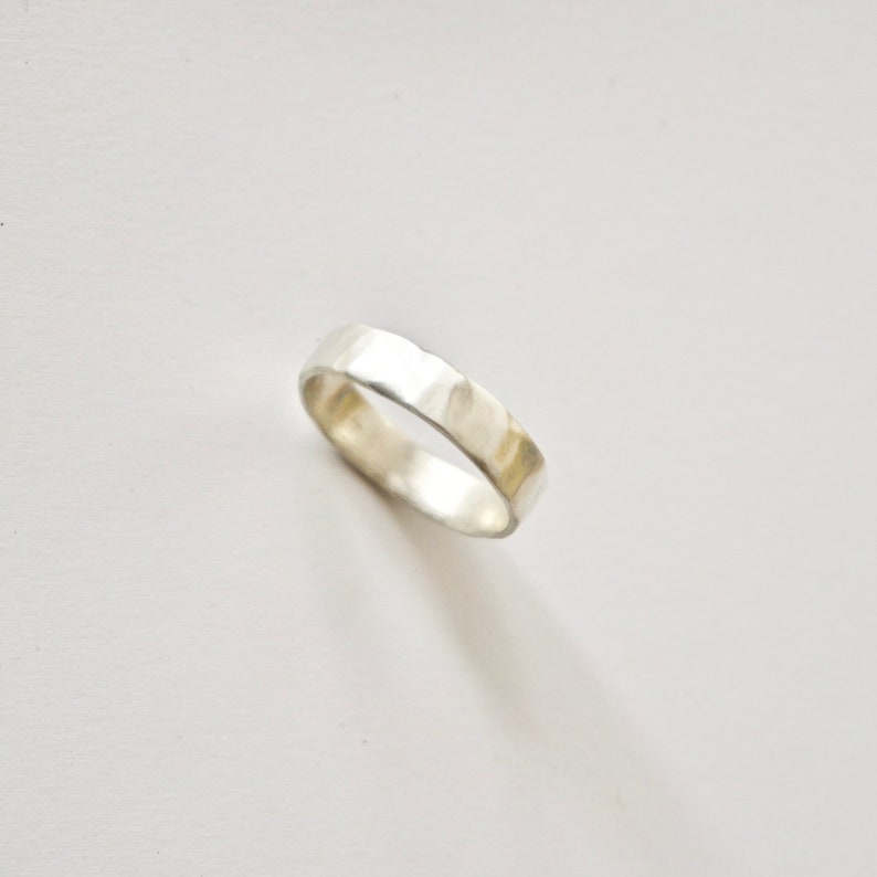 May include: A silver hammered band ring. The ring is smooth and has a slightly textured surface.
