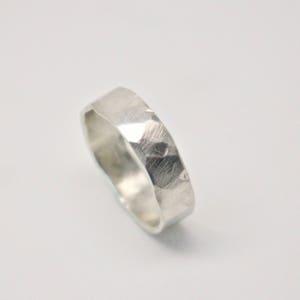 May include: A silver ring with a hammered texture. The ring has a flat band and a faceted surface, reflecting light. The ring is shown on a white background.