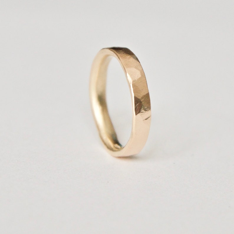 May include: A gold ring with a hammered texture. The ring has a simple band design and a slightly irregular surface. The ring is shown against a white background.