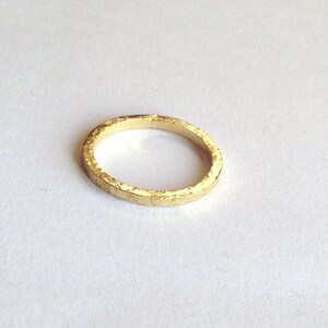 May include: A gold ring with a textured finish. The ring is circular and made of metal. The ring is set against a white background.