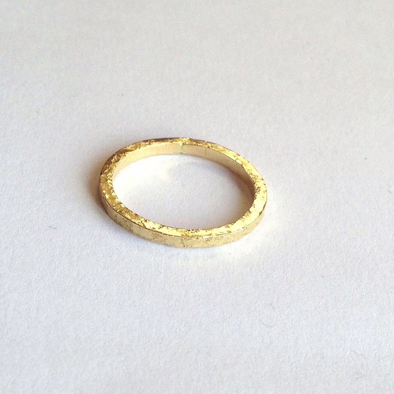 May include: A gold ring with a textured finish. The ring is circular and made of metal. The ring is set against a white background.