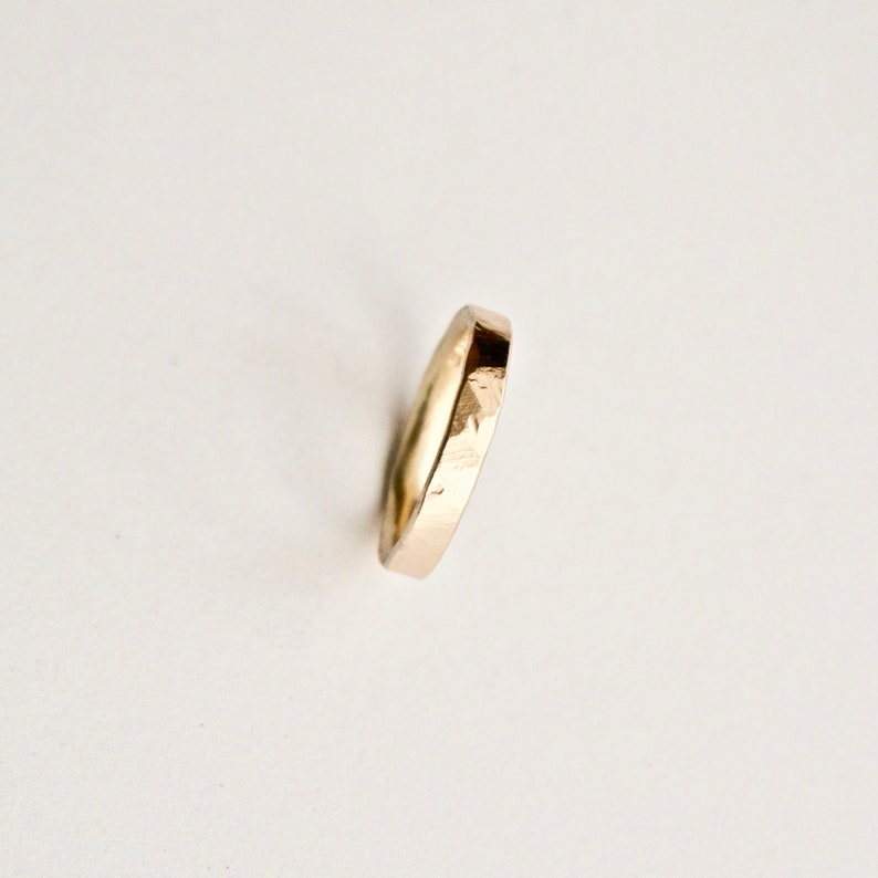 May include: A gold ring with a textured surface. The ring is a simple band design, with a slightly faceted appearance. The ring is set against a white background, highlighting its metallic sheen.