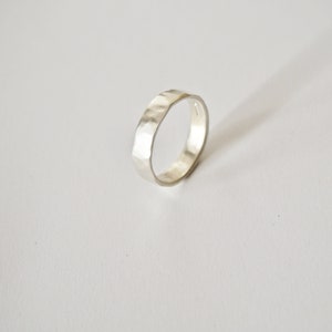May include: A silver hammered band ring. The ring is thick and has a textured surface.
