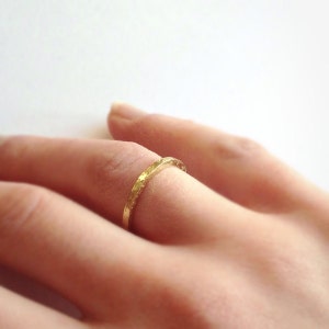 May include: A close-up of a gold ring with a textured surface. The ring is worn on a finger, showcasing its delicate design and craftsmanship. The ring's warm gold colour contrasts with the skin tone, highlighting its elegant simplicity.