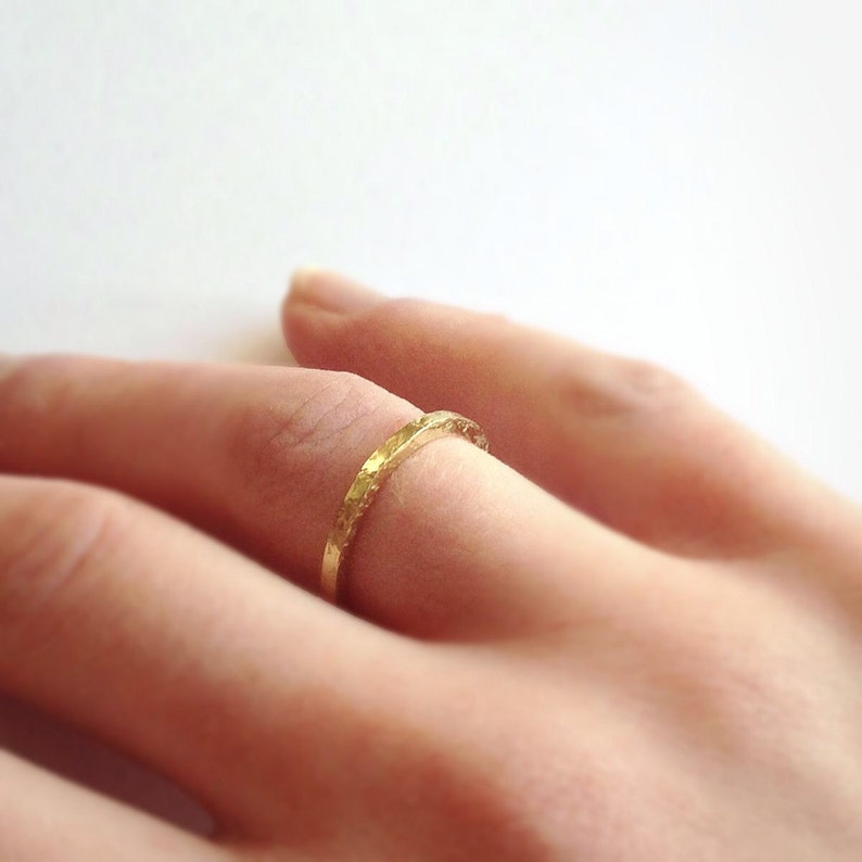 May include: A close-up of a gold ring with a textured surface. The ring is worn on a finger, showcasing its delicate design and craftsmanship. The ring's warm gold colour contrasts with the skin tone, highlighting its elegant simplicity.