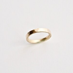 May include: A gold ring with a textured surface. The ring has a flat band and a slightly irregular shape, suggesting a handcrafted design. The ring is set against a plain white background.