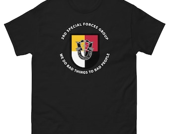 Puede incluir: Camiseta negra con un gráfico circular blanco que presenta el texto "3rd Special Forces Group" y "We do bad things to bad people". El gráfico también incluye un escudo con un diseño amarillo, rojo y blanco.