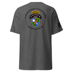 Może przedstawiać: Ciemnoszara koszulka z wojskowym emblematem na plecach. Emblemat zawiera tekst "2nd Ranger Battalion - 75th Ranger Regiment" i "Rangers Lead the Way". Projekt zawiera tarczę z błyskawicą, gwiazdą i słońcem.