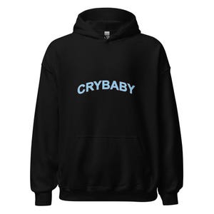May include: Black hooded sweatshirt with the word "CRYBABY" in light blue across the chest. The sweatshirt has a drawstring hood and a front pocket. A casual, comfortable garment.