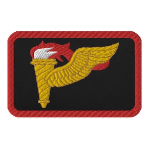 Puede incluir: Un parche bordado negro con borde rojo. El parche presenta una antorcha alada dorada con una llama roja.